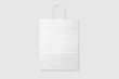 © PrimeMockup - Mockup of a blank white paper shopping bag with handles on light grey background. High resolution.
