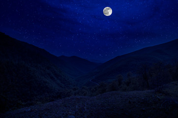Wall Mural - mountain road through the forest on a full moon night. scenic night landscape of country road at nig