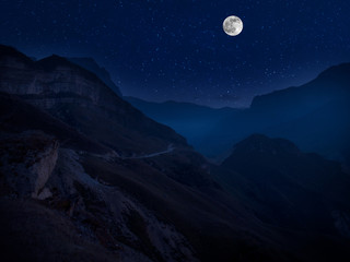 Wall Mural - mountain road through the forest on a full moon night. scenic night landscape of country road at nig