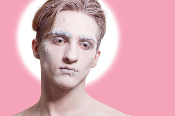 Beautiful young man with fashionable hair and make-up of snow on a pink background.