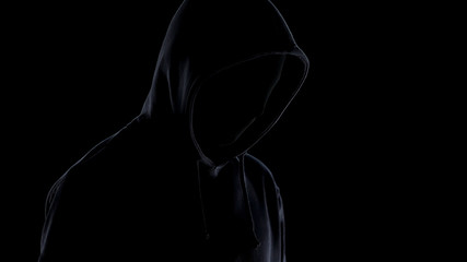 Dangerous maniac in mask and hoodie standing against black background, crime