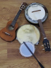 Four Brazilian musical instruments: cavaquinho, samba banjo, pandeiro (tambourine) and tamborim with drumstick on a wooden surface. The instruments are widely used to accompany samba music.