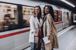 Two cheerful young women standing on subway platform