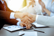 © rogerphoto - Business people shaking hands at meeting while theirs colleagues clapping and applauding. Group of unknown businessmen and women in modern white office. Success teamwork, partnership and handshake