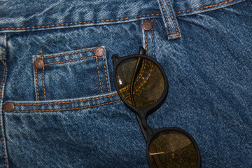 round sunglasses on a denim texture background. round yellow glasses in the front pocket of jeans. r