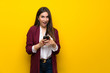© luismolinero - Young woman over yellow wall surprised and sending a message