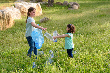 Wall Mural - Cute little girls cleaning up plastic litter on grass. Children Volunteers cleaning up litter and putting plastic bottle into recycling bag.