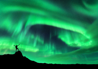 Wall Mural - aurora borealis and silhouette of a man with raised up arms on the mountain peak. lofoten islands, n