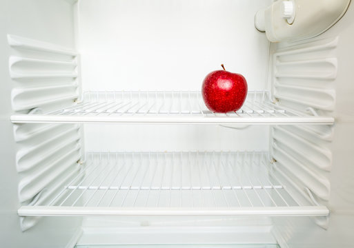 Bright fresh red apple on shelf of open empty refrigerator. Weight loss diet concept.