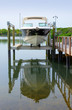 © Michael O'Keene - Small clean v-bottom bay motorboat on an electric lift on a wood dock with boat reflection in the clear blue water on sunny morning in tree lined bay shoreline.