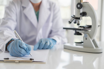 Wall Mural - a scientist hands writing on a clipboard in laboratory with test tube microscope and solutions.
