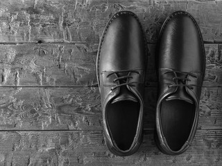 A pair of classic black leather men's shoes on a black wooden floor. The view from the top.