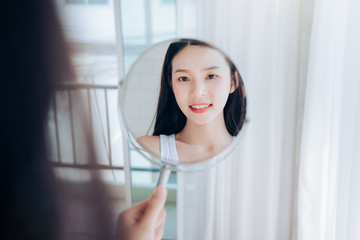 Wall Mural - Young Beauty Asian Woman Looking at Mirror Check Clear Face Skincare and Smile Morning in White Bedroom.