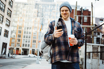 Wall Mural - Man walking on a sidewalk on the city street using mobile phone and cup of coffee to go