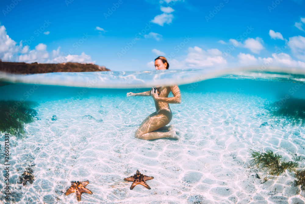 Naked woman swim in blue ocean with starfish, underwater in tropical sea - obrazy, fototapety, plakaty 
