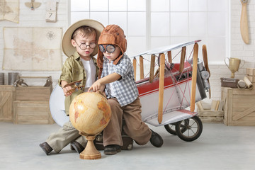 Little boys in the form of a pilot and a tourist play near the toy-plane in the room