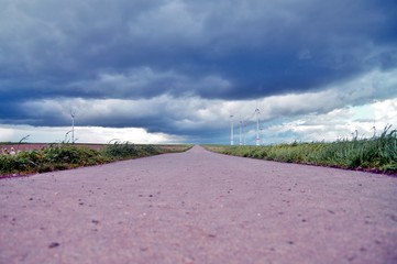 Wind turbines in green landscape, rural road between green fields or grassland, before the Thunder-storm, alternative energy, new natural scenery 