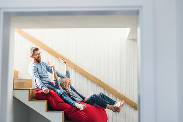 Wall Mural - An adult hipster son and senior father indoors at home, having fun.