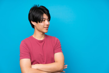 Wall Mural - Asian man with red shirt over isolated blue wall standing and looking to the side