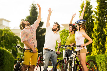 Four happy friends resting outdoors. Group of smiling cyclists resting in summer park. Best weekend with friends.