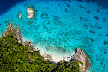 Aerial drone view of a lush tropical island with crystal clear water surrounded by coral reef