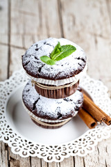 Wall Mural - Chocolate dark muffins with sugar powder, cinnamon sticks and mint leaf on white plate on rustic wooden table.