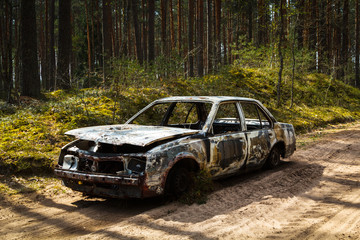 Fully burnt car in the forest in spirng on sandy road