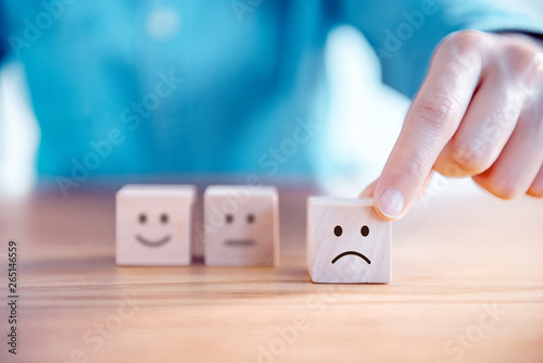 Fotografía Close up customer hand choose sad face and blurred smiley face icon on wood cube, Service rating, satisfaction concept