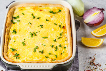 Canvas Print - Onion pie with cheese and herbs in black baking dish.