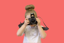 A Little Girl In Business Clothes Holds A Reflex Camera In Her Hands In Front Of Her Face. The Child Wants To Take A Picture. The Baby Learns To Take Pictures And Studies The Complex Technique
