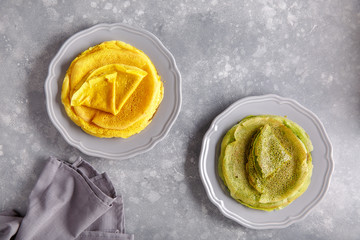 Wall Mural - Yellow and green pancakes on gray plate.  Stack of spinach crepes and crepes tinted turmeric on concrete background. Top view, copy space.