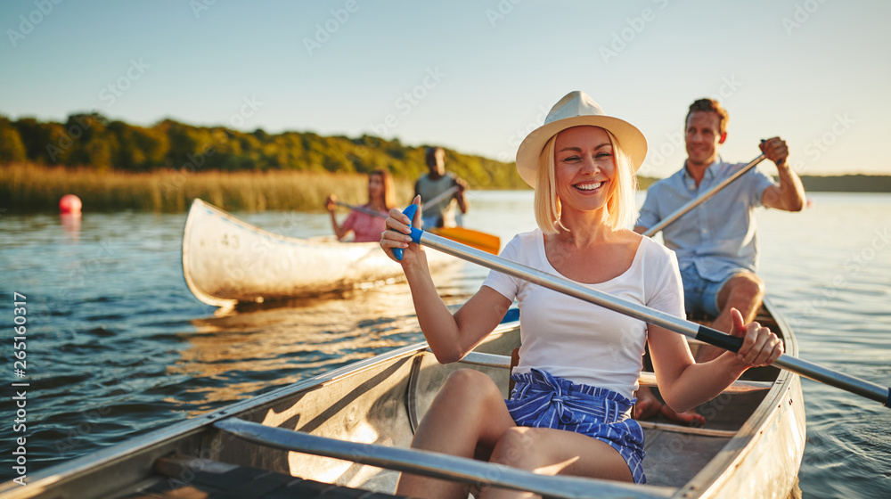 Laughing young woman canoeing with friends on a sunny afternoon - obrazy, fototapety, plakaty 