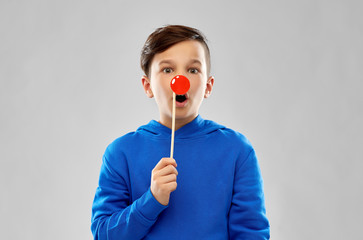 Wall Mural - red nose day, party props and photo booth concept - shocked boy in blue hoodie with clown nose over grey background