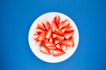 Sticker - Fresh juicy cut strawberries on a white plate on blue background. Flat lay style.