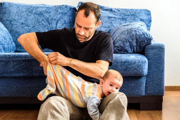 Wall Mural - Novice father changing clothes to his baby with effort in the living room of his house.