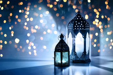 Wall Mural - Couple of glowing Moroccan ornamental lanterns on the table. Greeting card, invitation for Muslim holy month Ramadan Kareem. Festive blue night background with glittering golden bokeh lights.