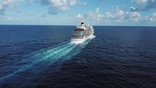 Back Of The Cruise Ship And Its Beautiful Wake On The Blue Sea Surface, Seascape. Stock. Aerial View Of A Beautiful White Cruise Liner In A Sunny Day On Blue Cloudy Sky Background.