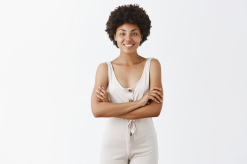 Powerful and successful African American woman being in great mood standing in gray overalls with hands on chest, smiling broadly at camera, feeling well and independent over grey background