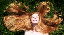 Portrait Of A Beautiful Young Sexy Red-haired Woman, Lying In The Spring Sun In Happiness,  Relaxing On The Green Grass, The Red Hair Draped Freely Around The Head.