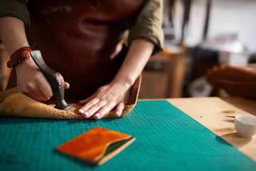 Wall Mural - Warm toned close up of female artisan making leather bag in leatherworking atelier, copy space