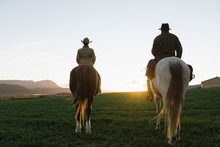 Back View Of Man And Woman Riding Horses Against Sunset Sky On Ranch