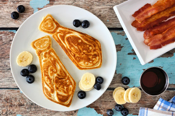 Poster - Tie shaped pancakes with blueberries and bananas. Fathers Day breakfast concept. Top view table scene on a rustic blue wood background.