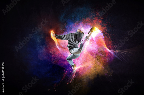 Modern female dancer jumping in hoodie with colourful splashes background. Mi...