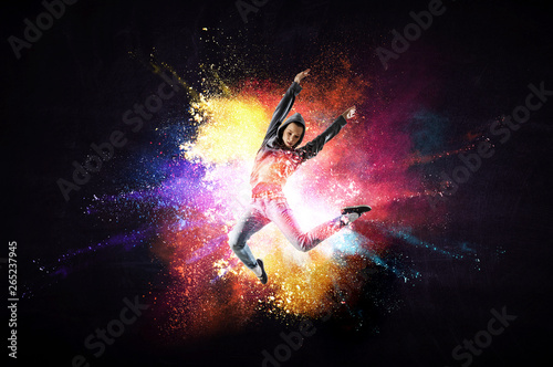 Modern female dancer jumping in hoodie with colourful splashes background. Mi...