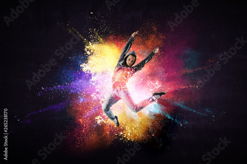 Modern female dancer jumping in hoodie with colourful splashes background. Mi...