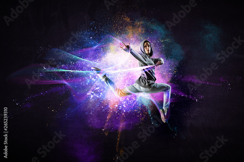 Modern female dancer jumping in hoodie with colourful splashes background. Mi...