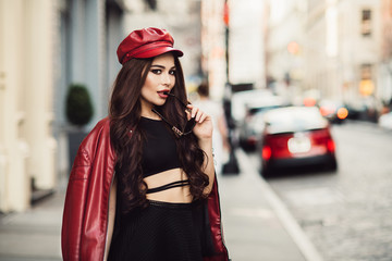 Wall Mural - Beautiful fashionable sexy woman with makeup posing on city street wearing a red jacket, hat and sunglasses.