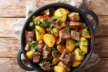 homemade food of fried pork with potatoes and mushrooms close-up in a frying pan. horizontal top vie