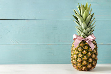 Ripe fruit pineapple with a pink bow on a blue wooden background. space for text