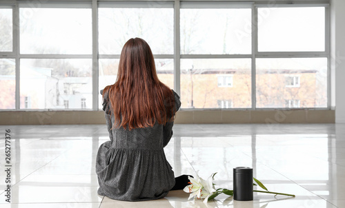 Cuadros en Lienzo Woman with mortuary urn and lily flowers sitting in empty room, back view